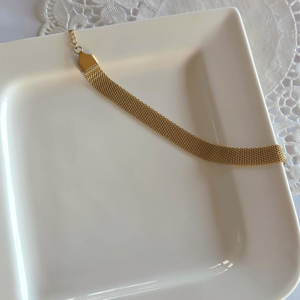 Gold necklace on a white dish with a lace tablecloth background