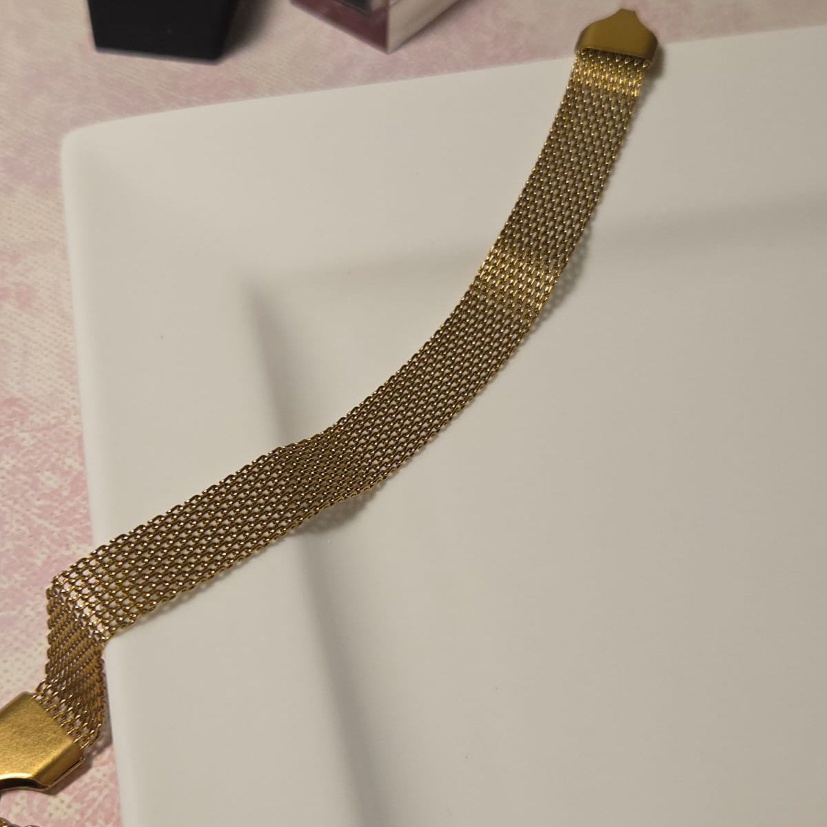 Gold chain necklace on a white surface with a pink background
