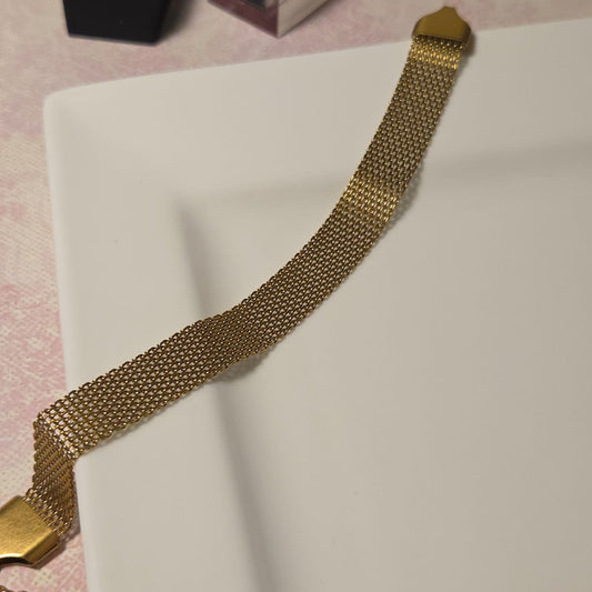 Gold chain necklace on a white surface with a pink background