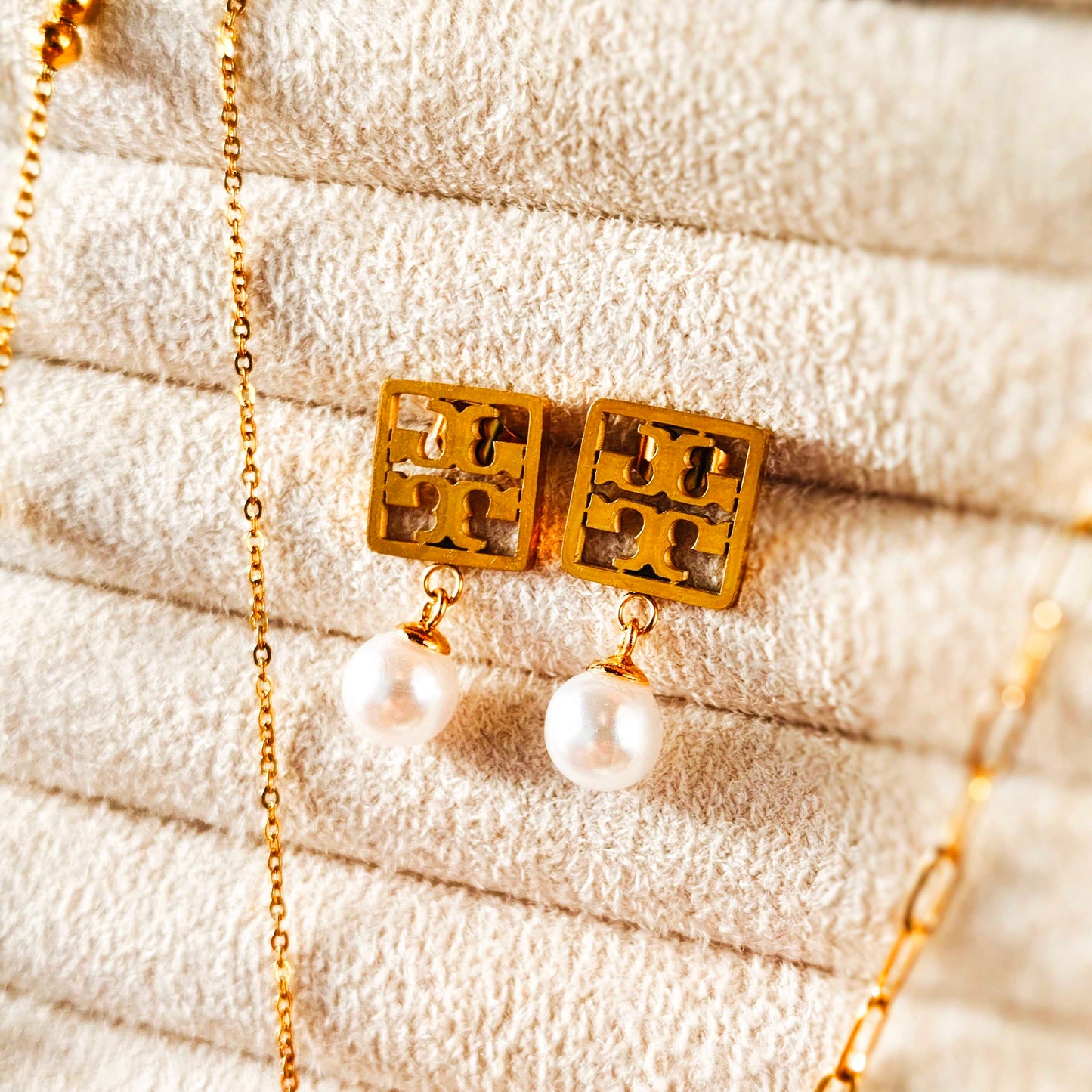 Gold earrings with pearl drops on a textured beige surface