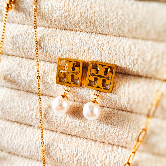 Gold earrings with pearl drops on a textured beige surface