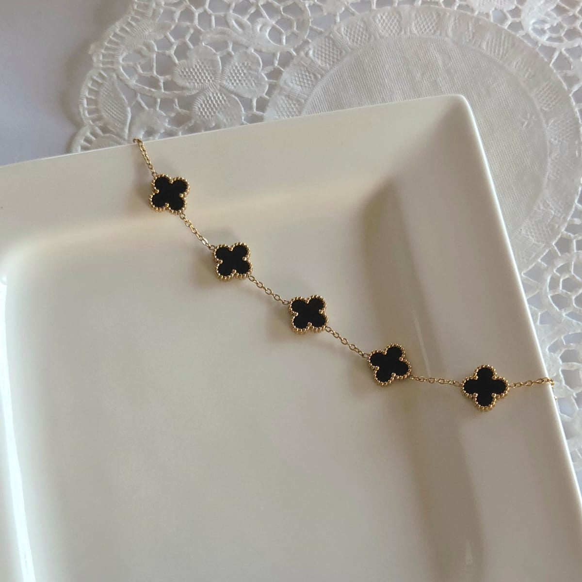 Gold necklace with black clover-shaped pendants on a white dish.