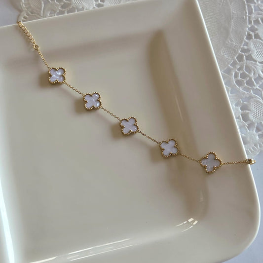Gold necklace with clover-shaped pendants on a white plate with a lace tablecloth background